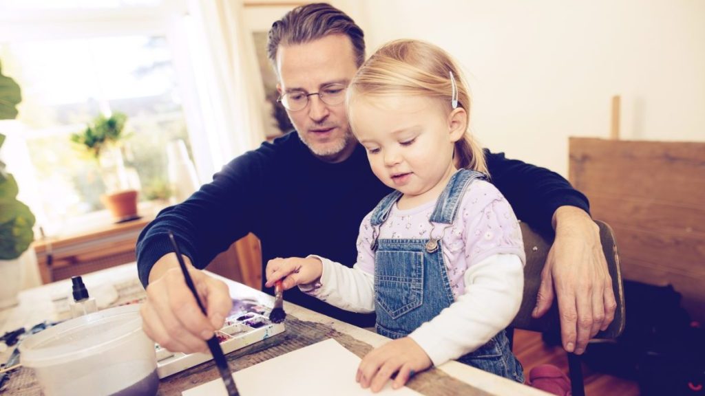 Father and her toddler daughter painting together with watercolor paint.