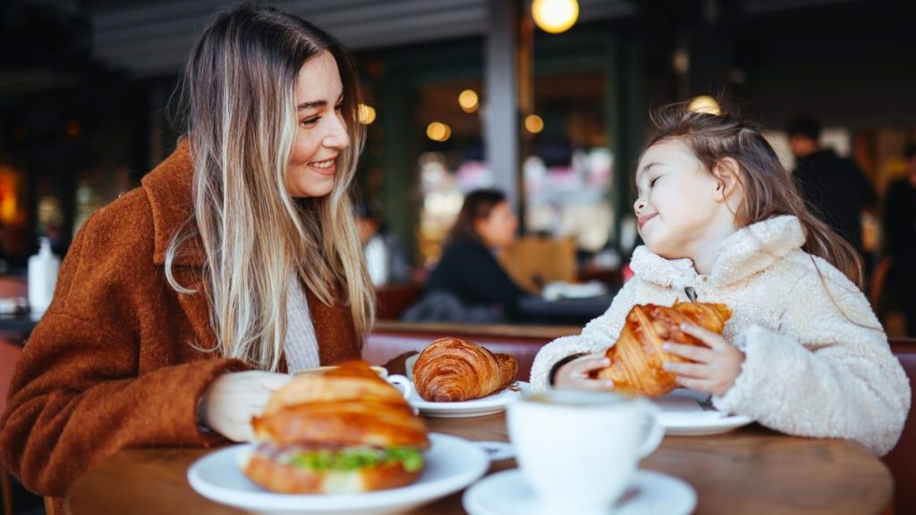 The happy girl has breakfast with mother in cafe on the street.