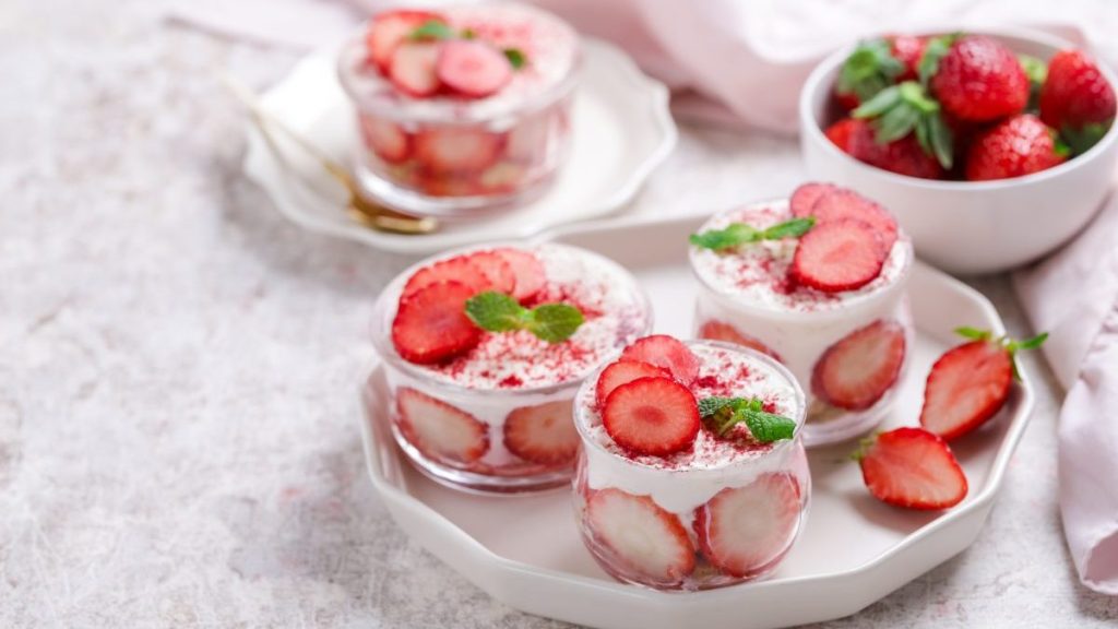 Strawberry trifle, dessert in a glass jar with fresh strawberry and mint leaves on a gray background