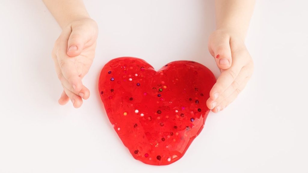 Red slime in a heart shape in a kid's hands. Love and Valentine's Day concept.