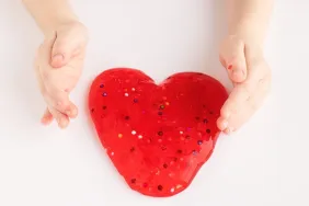 Red slime in a heart shape in a kid's hands. Love and Valentine's Day concept.