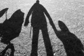 Shadow on lawn of a father, a small child and a baby carriage.