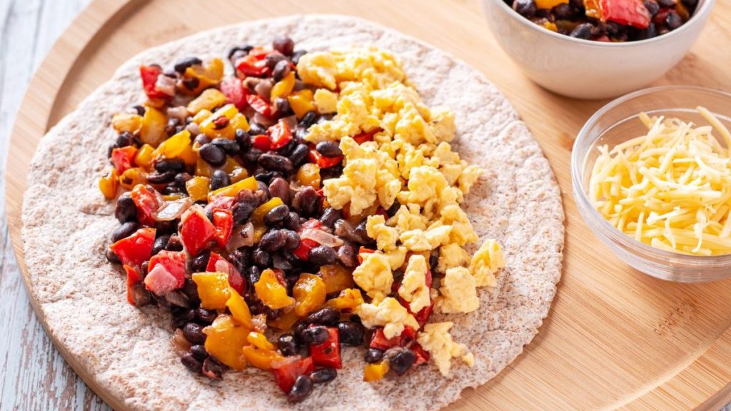 Healthy high protein burritos with eggs, bell peppers, sweet potato, black beans on whole wheat tortillas with grated cheese, top view.
