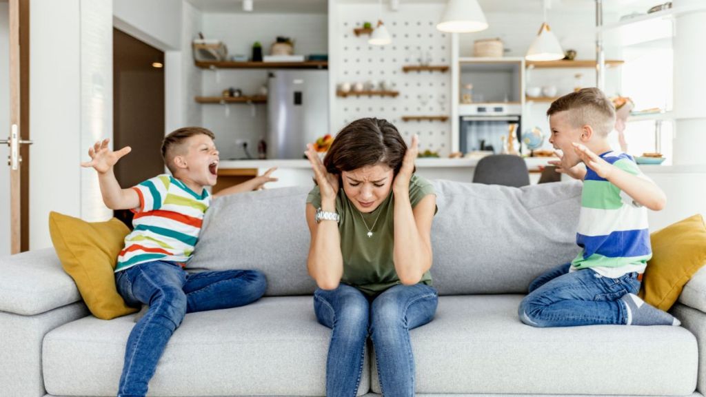 Stressed exhausted mother feeling desperate about screaming stubborn kids tantrum, upset annoyed mother tired of naughty difficult child boys misbehave yelling for attention.