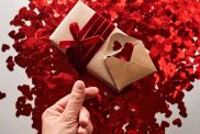 Craft gift and envelope with many red shiny hearts. Hand with thumb and index finger shows heart symbol in asia. A wonderful photo for Valentine's Day.