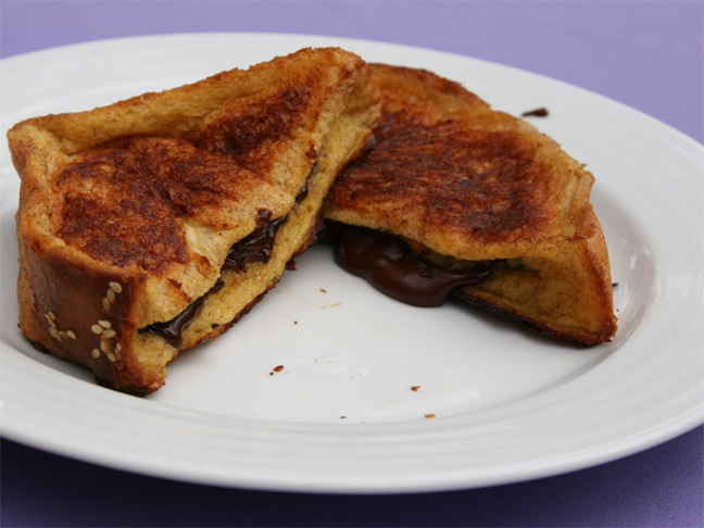 Two slices of Nutella baked french toast on a white plate with purple background